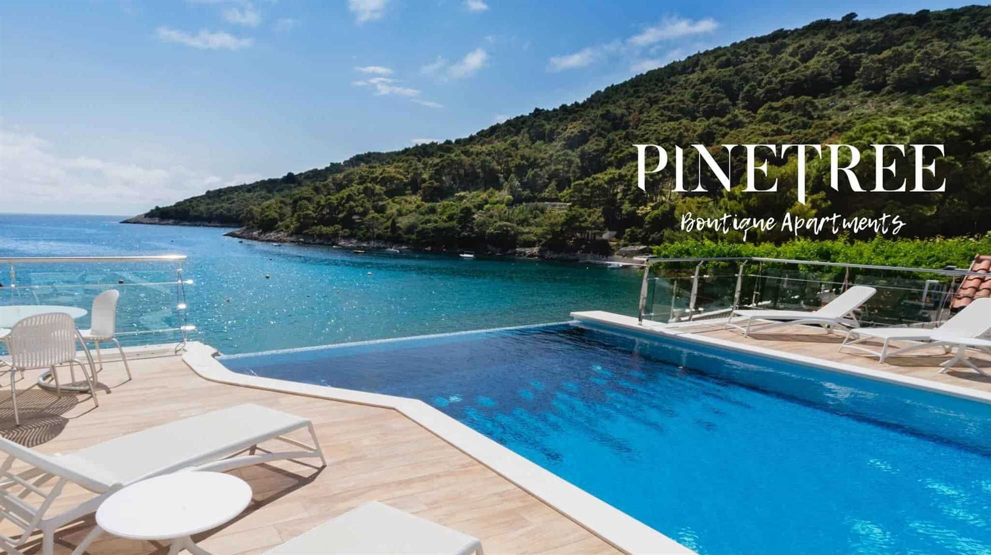Área da piscina com espreguiçadeiras e mesas, com vista para um mar azul cristalino e um morro arborizado.