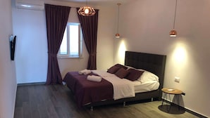 A modern bedroom with a large bed, dark wood flooring, and a small round table.