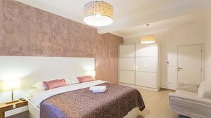 A modern hotel room with a large bed, a wardrobe, and a seating area.