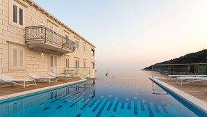 A poolside area with lounge chairs, a clear view of the sea, and a building with balconies.