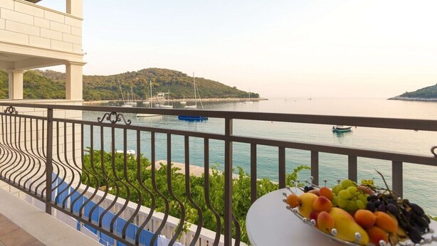 A balcony with a railing overlooking a body of water, a boat, and a distant hill.