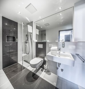 A modern bathroom with a glass-enclosed shower, a white toilet, and a sink with a mirror above it.