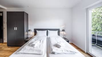 A modern bedroom with a large bed, two bedside tables, a wardrobe, and a balcony with a railing.