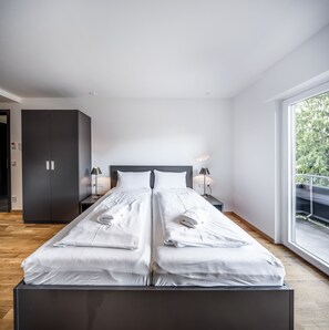 A modern bedroom with a large bed, two bedside tables, a wardrobe, and a balcony with a railing.