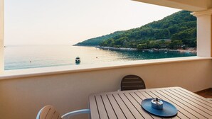 Un balcón con mesa y sillas con vista al mar tranquilo y una ladera verde.