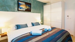 Una habitación de hotel con una cama grande, cabecero, mesita de noche, lámpara, un cuadro en la pared y un armario.