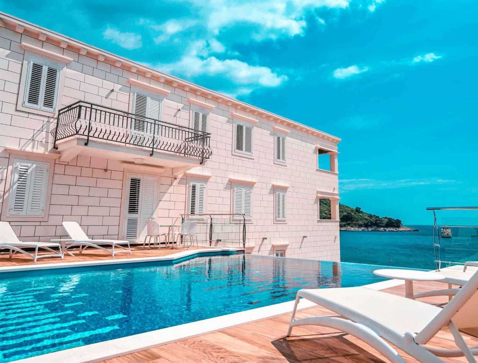 Un hôtel doté d’une piscine, de chaises longues blanches et offrant une vue sur la mer.