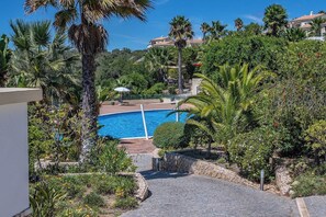 A pool surrounded by lush greenery and a stone pathway leading to a white building.