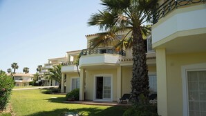 Un hotel con varios balcones, palmeras y un césped bien cuidado.