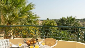 Mesa redonda con sillas y una mesa para el desayuno en una terraza con vistas a palmeras y colinas.