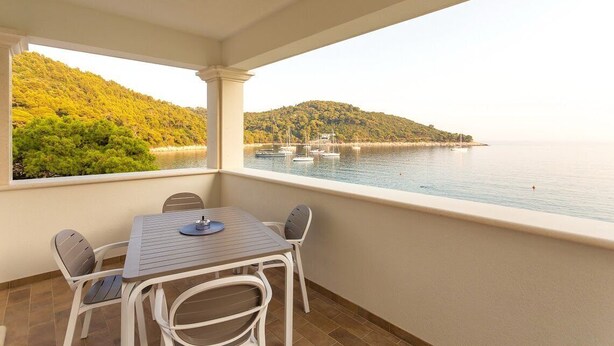 A balcony with a table and chairs, overlooking a body of water with boats and a hilly landscape. - Superior suite with sea view :) PRECIOUS MOMENTS (Mljet)