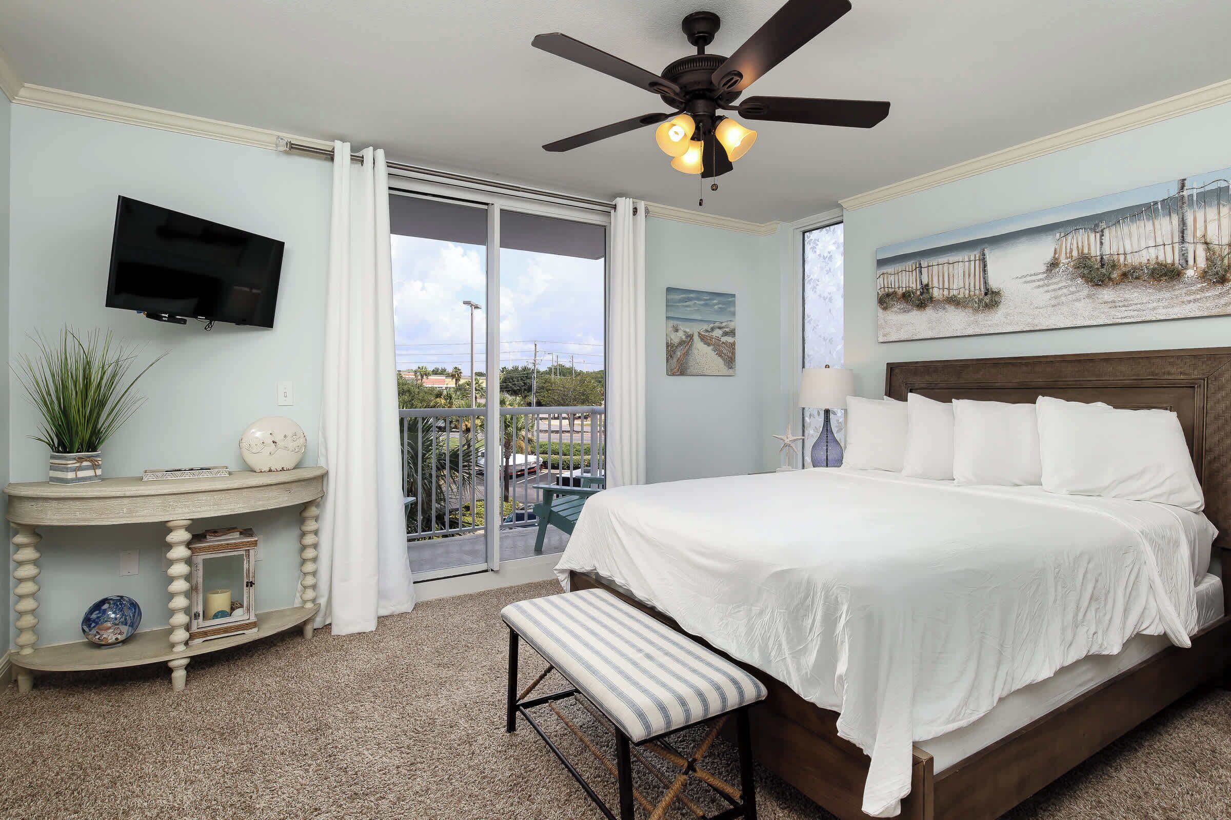 A bedroom with a bed, a desk, a bench, a ceiling fan, and a TV.