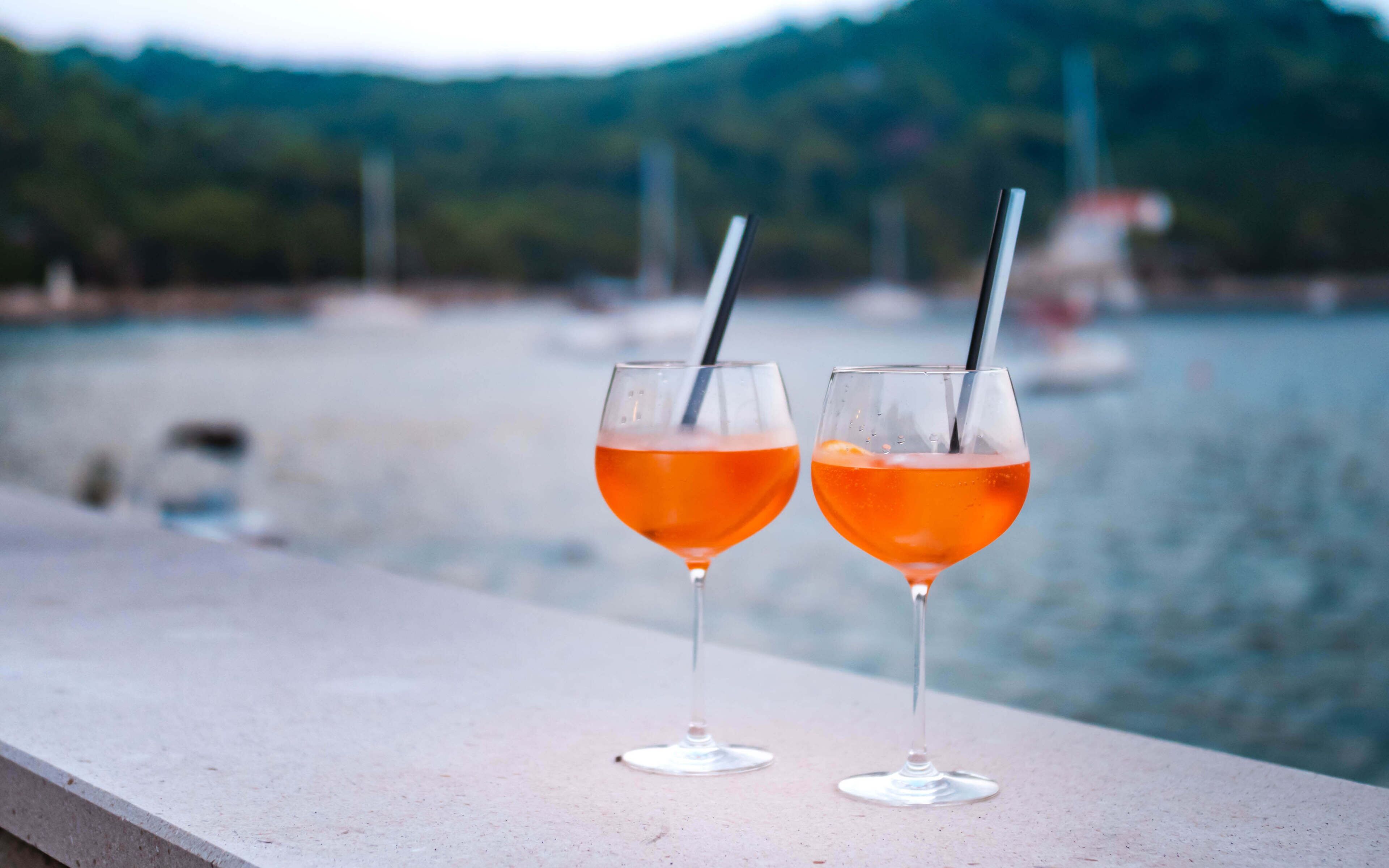 Deux verres contenant un liquide orange sont posés sur une étagère, près d’une étendue d’eau.