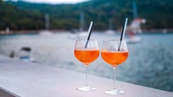Deux verres contenant un liquide orange sont posés sur une étagère, près d’une étendue d’eau.