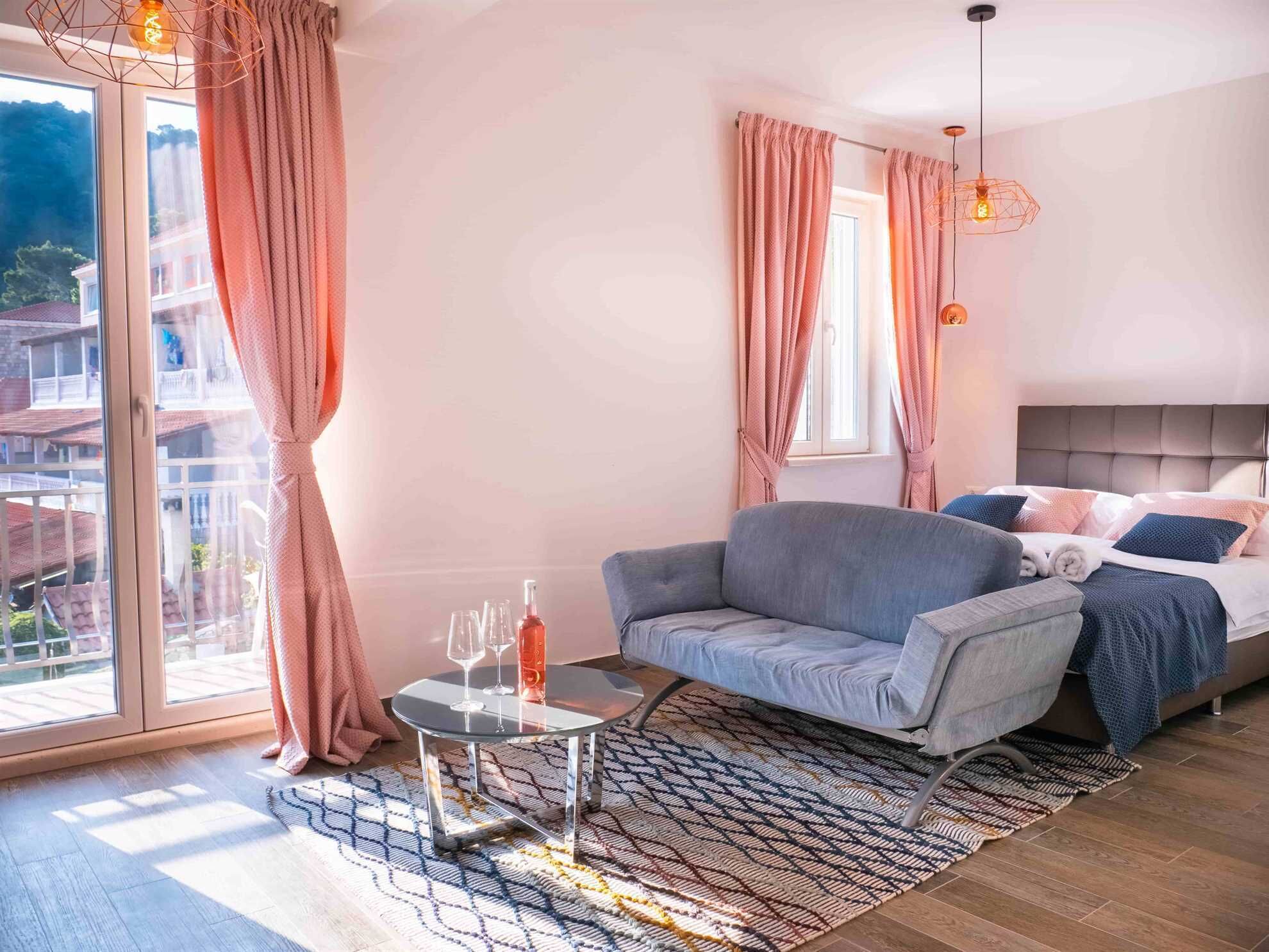 Une chambre moderne avec un canapé gris, une table basse en verre et un lit agrémenté de plusieurs coussins.