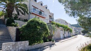A residential street with stone buildings, a palm tree, and a clear sky.