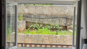 A hotel room with a large window overlooking a stone wall and greenery.