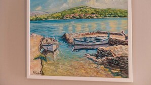 Pintura emoldurada de uma paisagem costeira com barcos e uma colina ao fundo.
