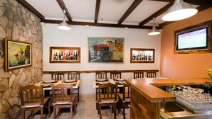 Um restaurante com mesas e cadeiras de madeira, parede de pedra e obras de arte emolduradas nas paredes.