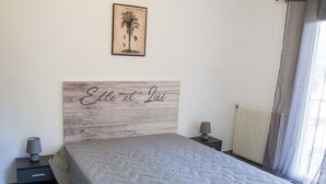 Una camera da letto con un letto, un comodino, una lampada, un termosifone e una finestra con tende.