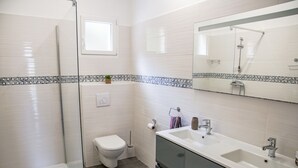 Un bagno moderno con cabina doccia in vetro, un water, un lavandino con specchio e una schiena di cucina in piastrelle.