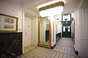 A hallway with a large mirror, a door with a gold frame, and a patterned floor.