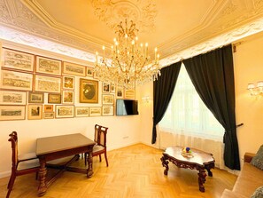 A room with a dining table, chairs, a chandelier, framed pictures on the wall, and a television.