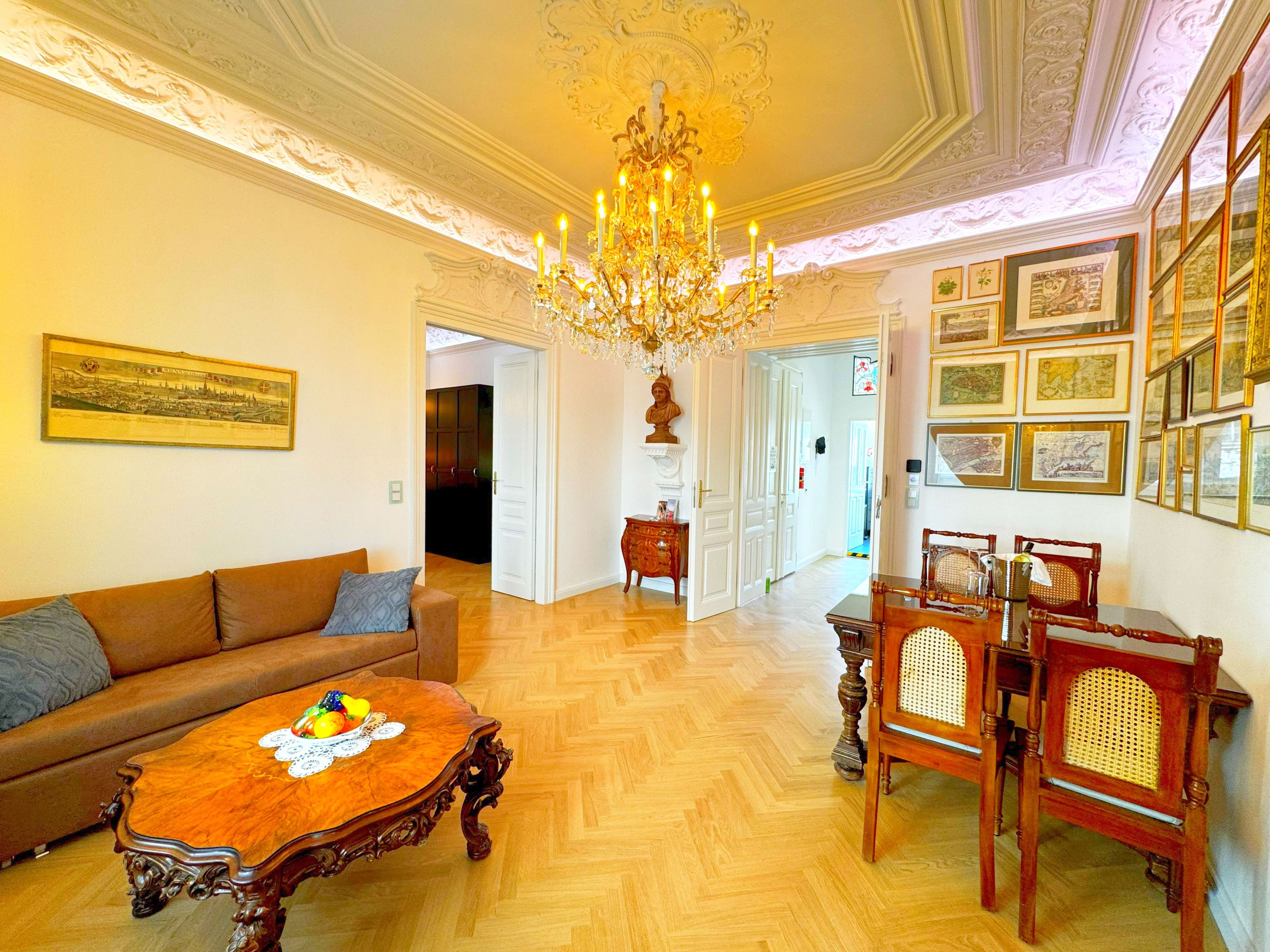 A room with a chandelier, a wooden dining table with chairs, a sofa, and a framed picture on the wall.