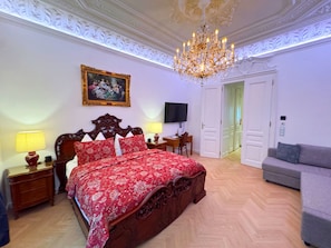 A bedroom with a large bed, a desk, a television, and a sofa.