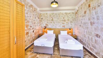 Una habitación con dos camas, un armario, paredes de piedra y un candelabro.