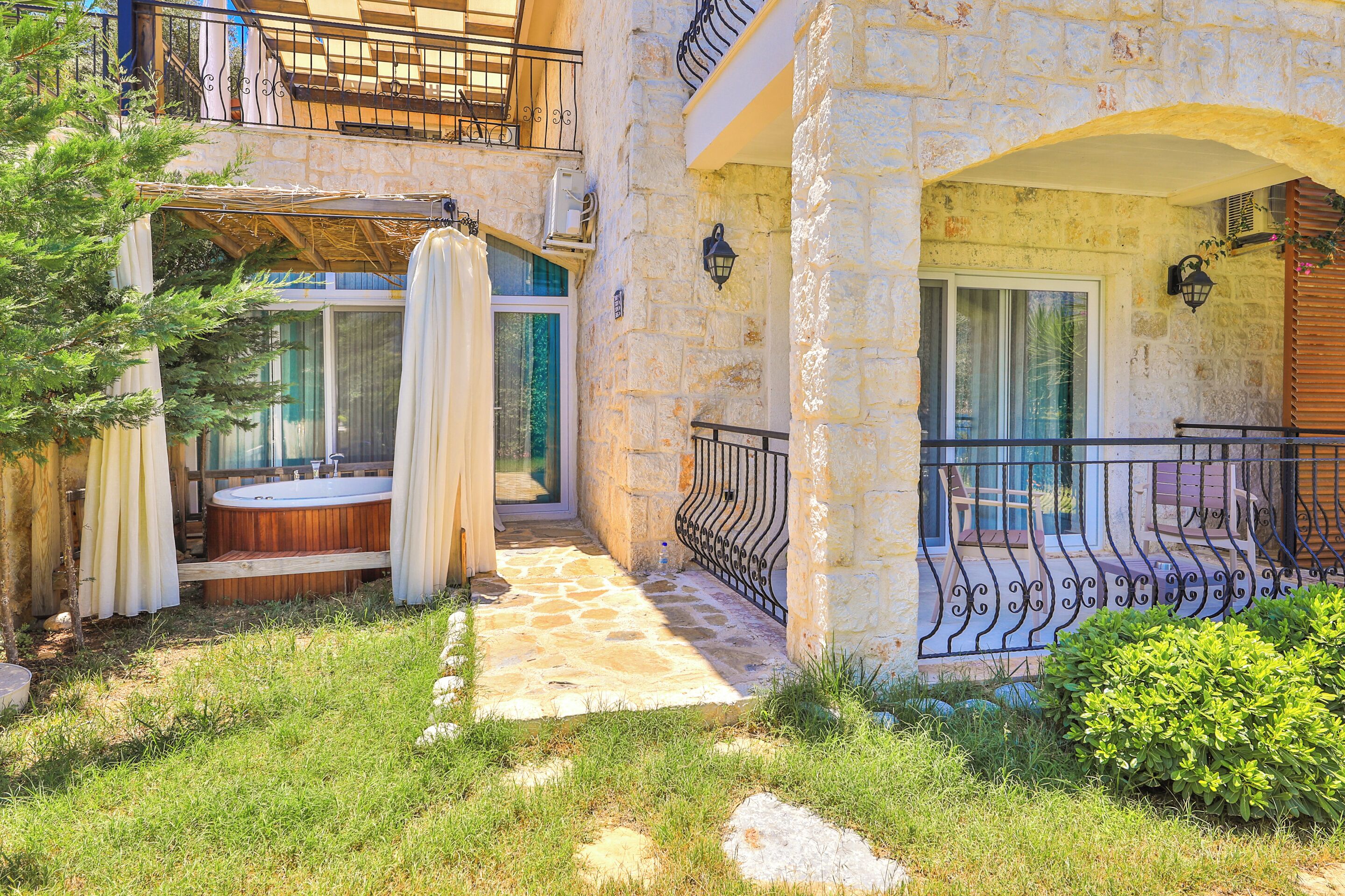A stone building with a wooden deck, a hot tub, and a balcony with a wrought iron railing.