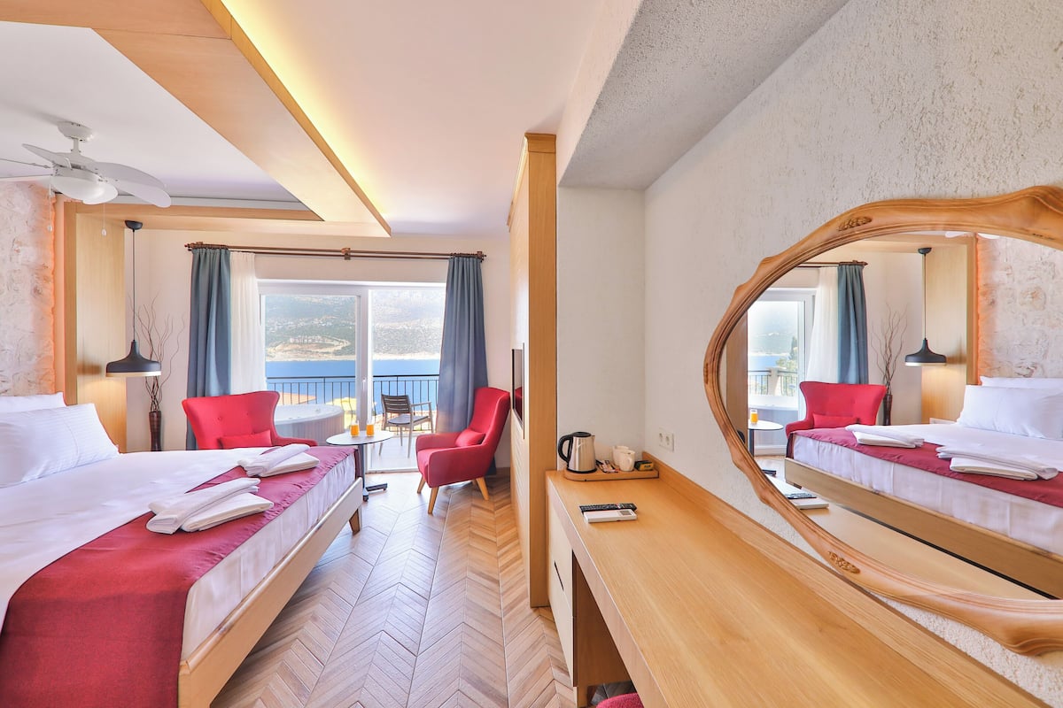 A hotel room with two beds, a desk, a chair, a large mirror, and a balcony with a view.