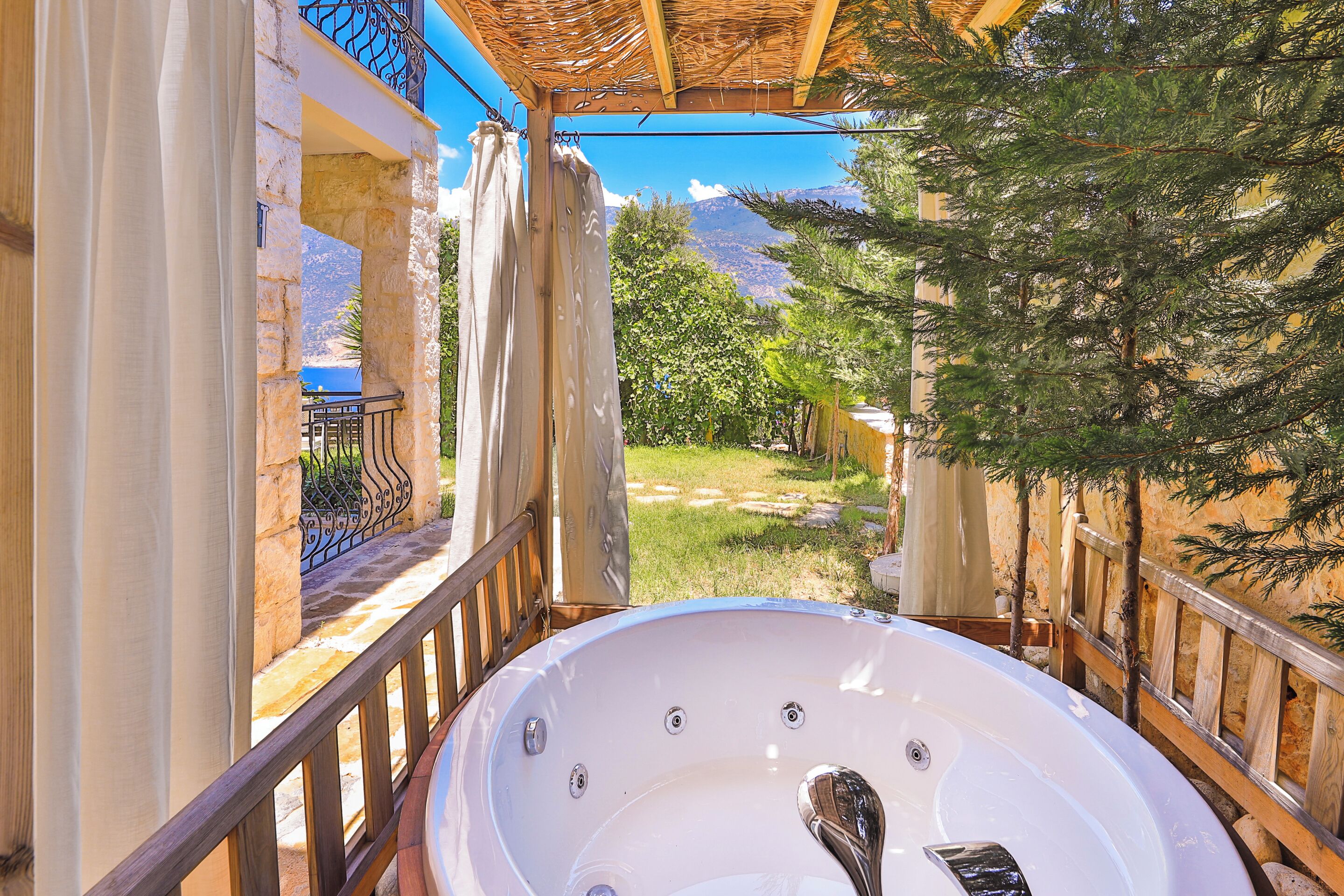 A hot tub under a pergola with a view of a mountainous landscape.