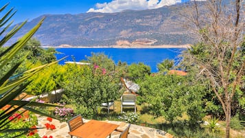 A patio with a table and chairs, overlooking a coastal landscape with mountains and a clear blue sea.