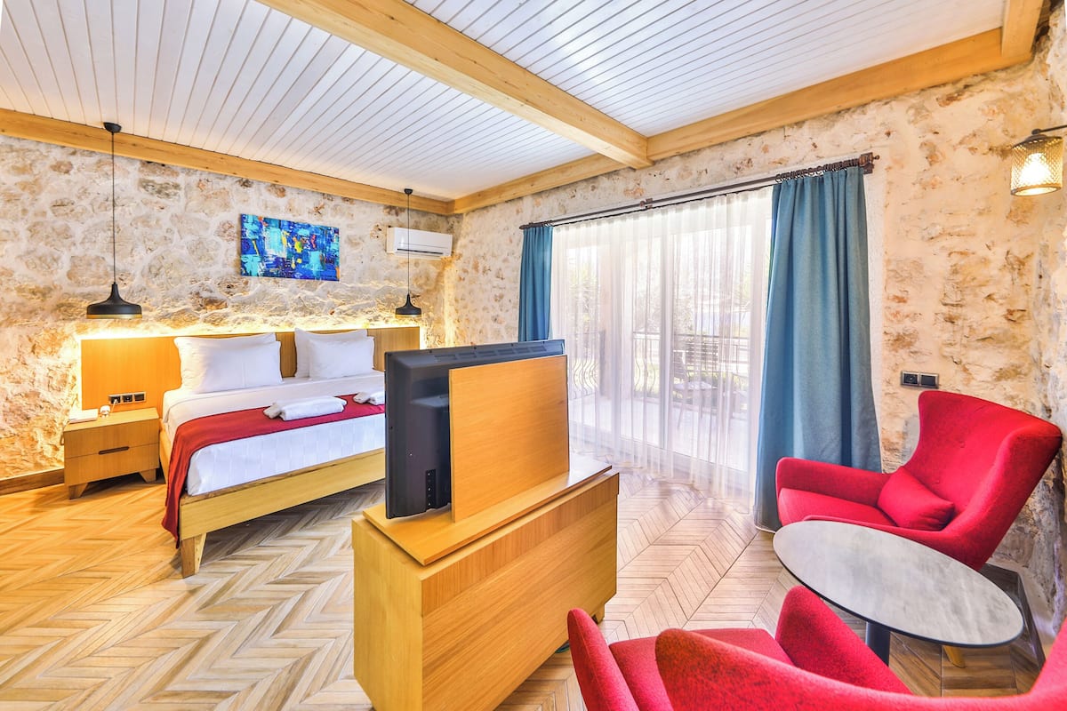 A hotel room with a wooden bed, a TV on a wooden stand, a red chair, and a large window with curtains.