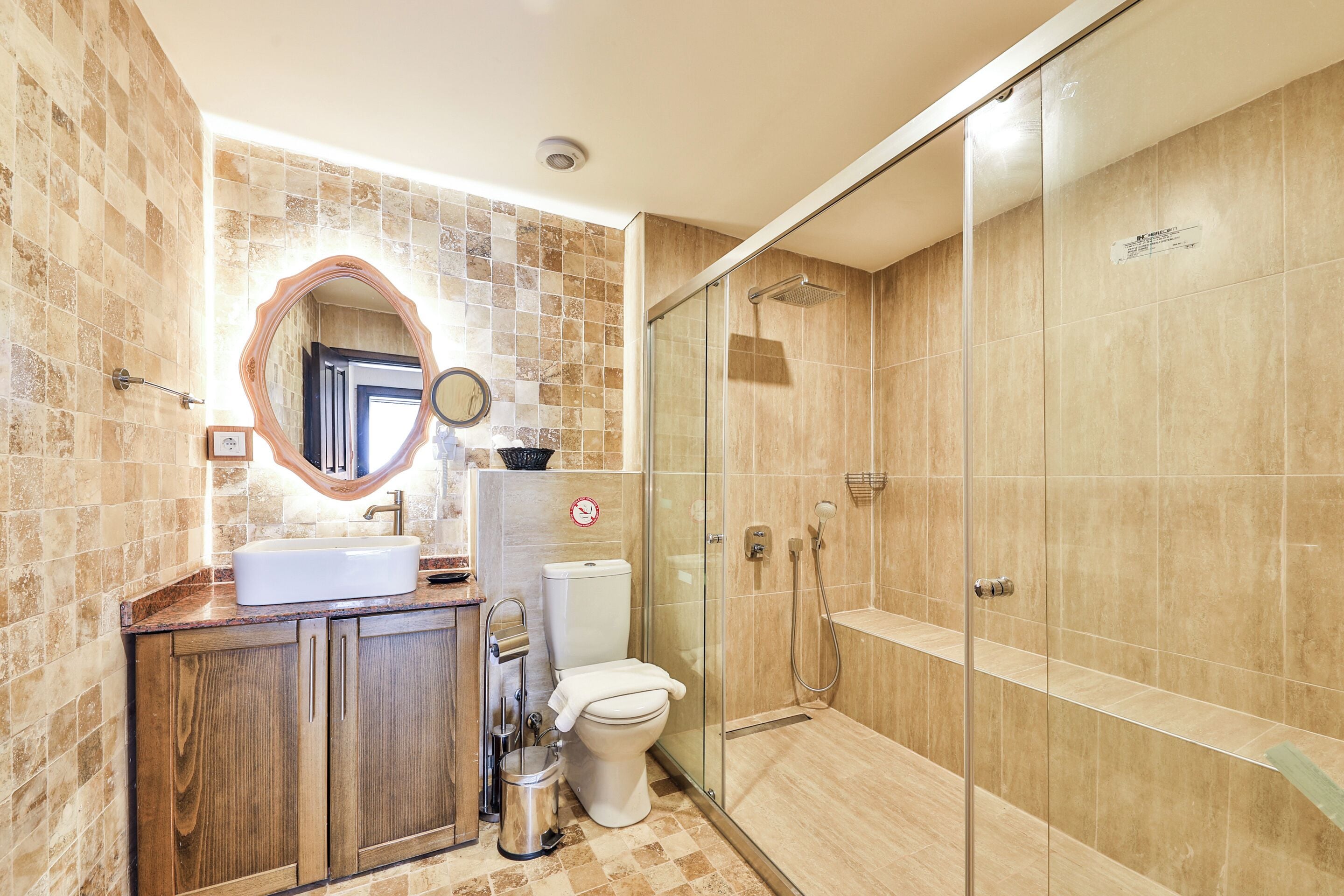 Een badkamer met een houten wastafelmeubel, een witte wastafel, een toilet en een douchecabine met glazen wanden.