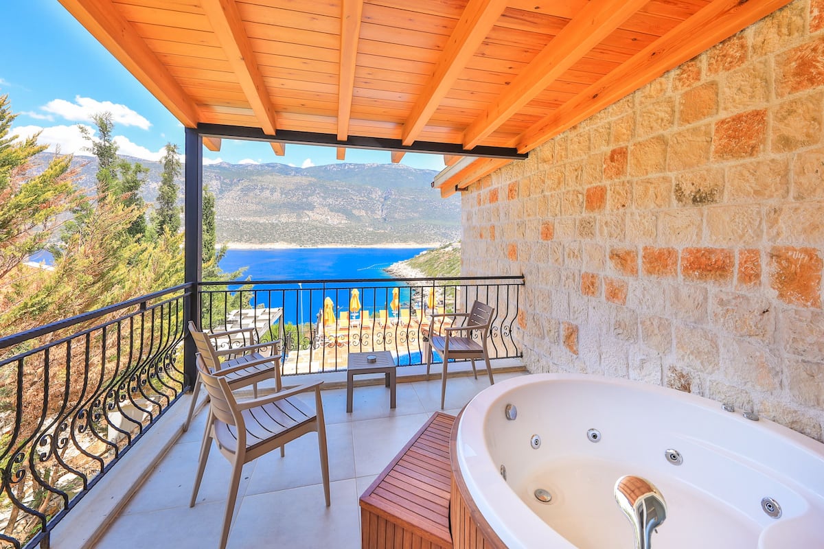A balcony with a wooden ceiling, stone wall, and a view of the sea.