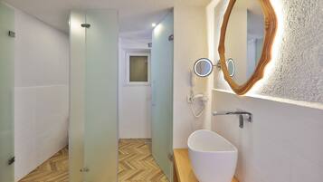 Un baño moderno con entrada de vidrio, un lavamanos blanco con encimera de madera y un espejo con marco de madera.
