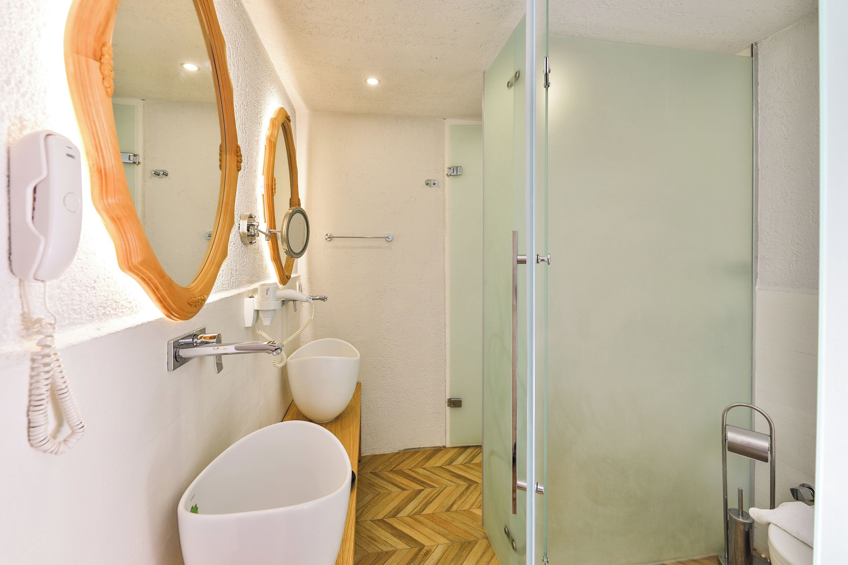 A bathroom with a white sink, two mirrors, a glass shower door, and a towel rack.