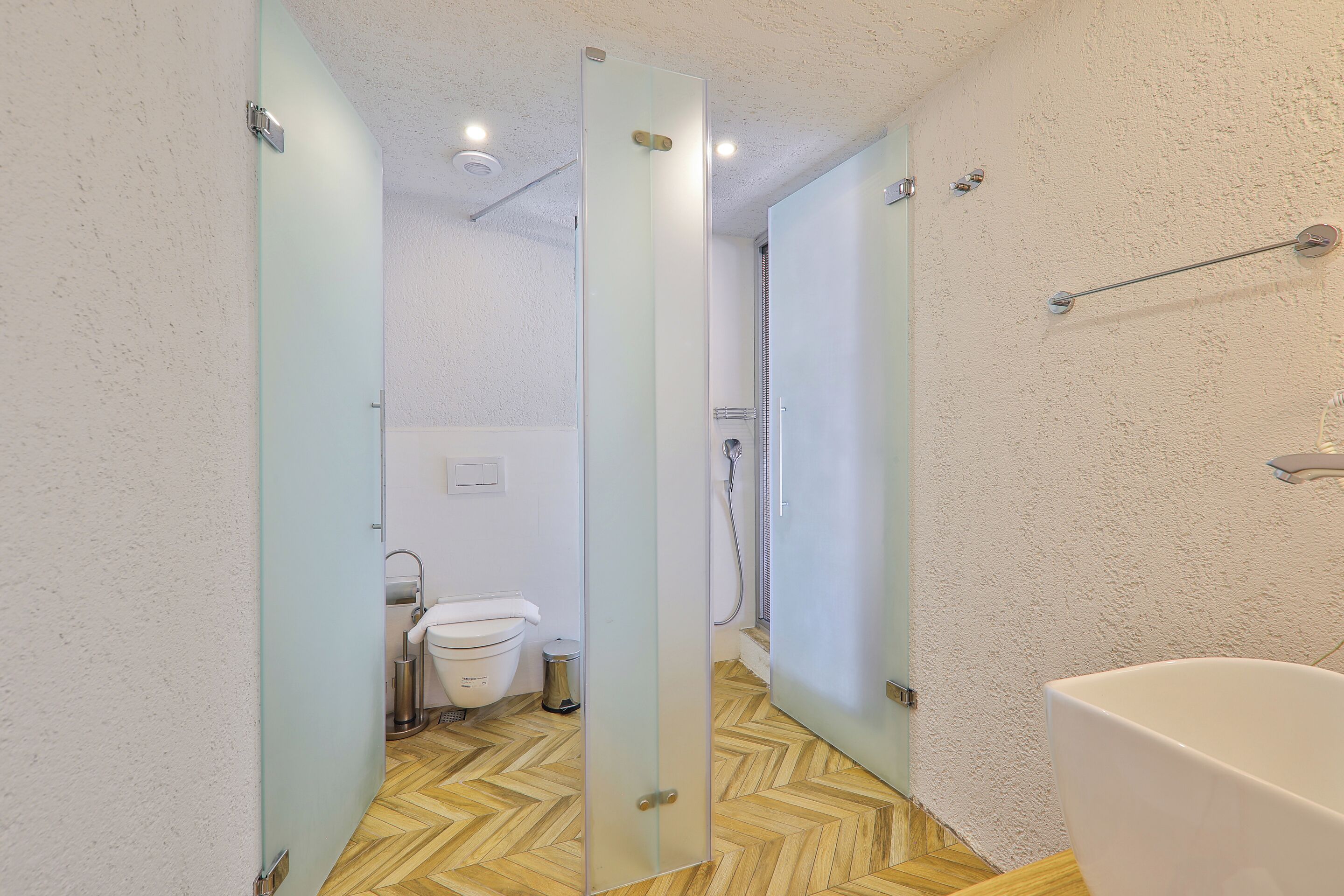 A bathroom with a wooden herringbone floor, a white bathtub, and a glass shower enclosure.