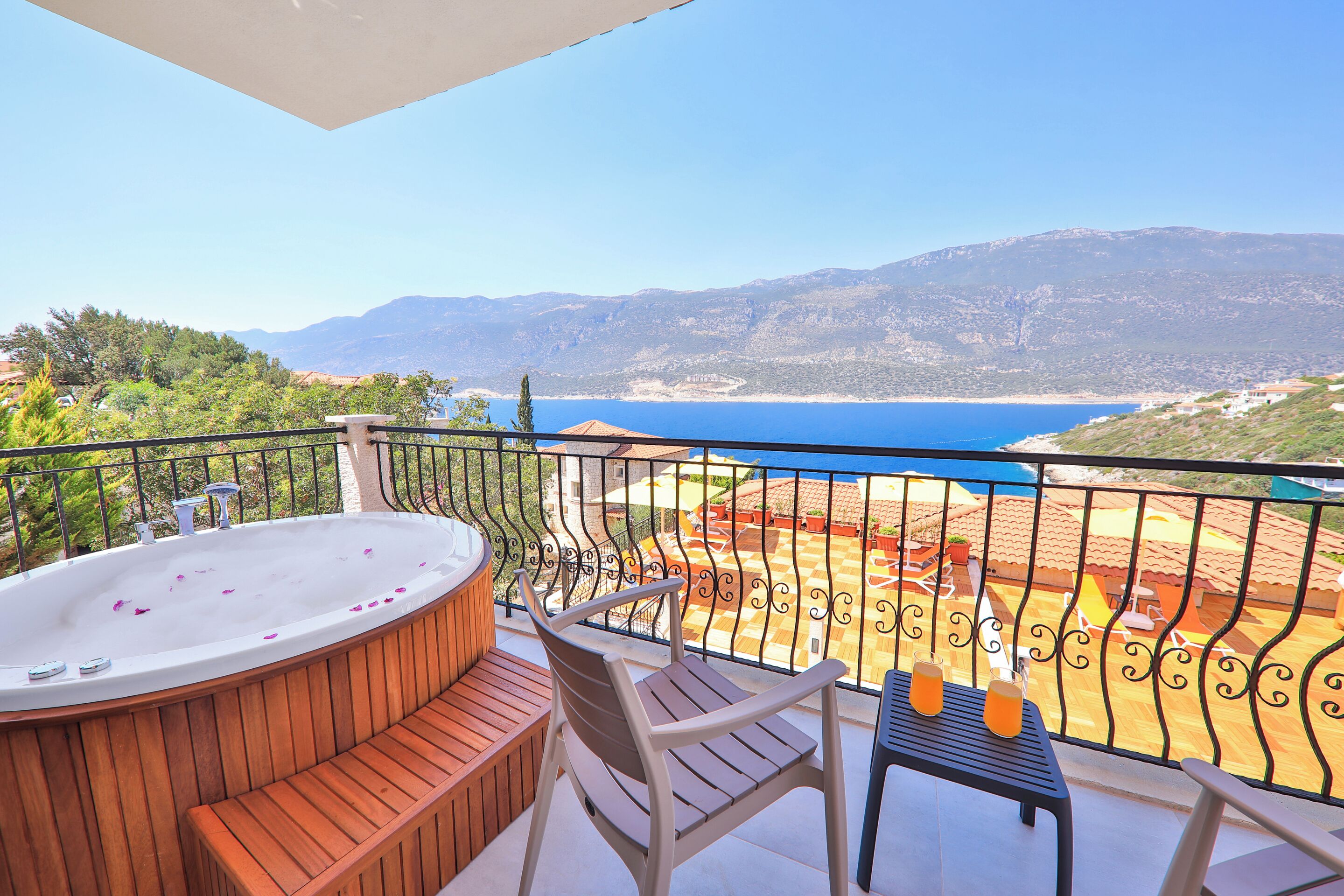A balcony with a hot tub, wooden seating, and a table with drinks.