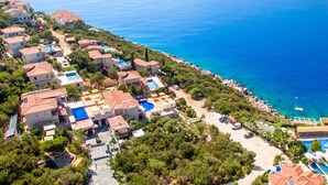 An aerial view of a coastal residential area with houses, a swimming pool, and a beach.