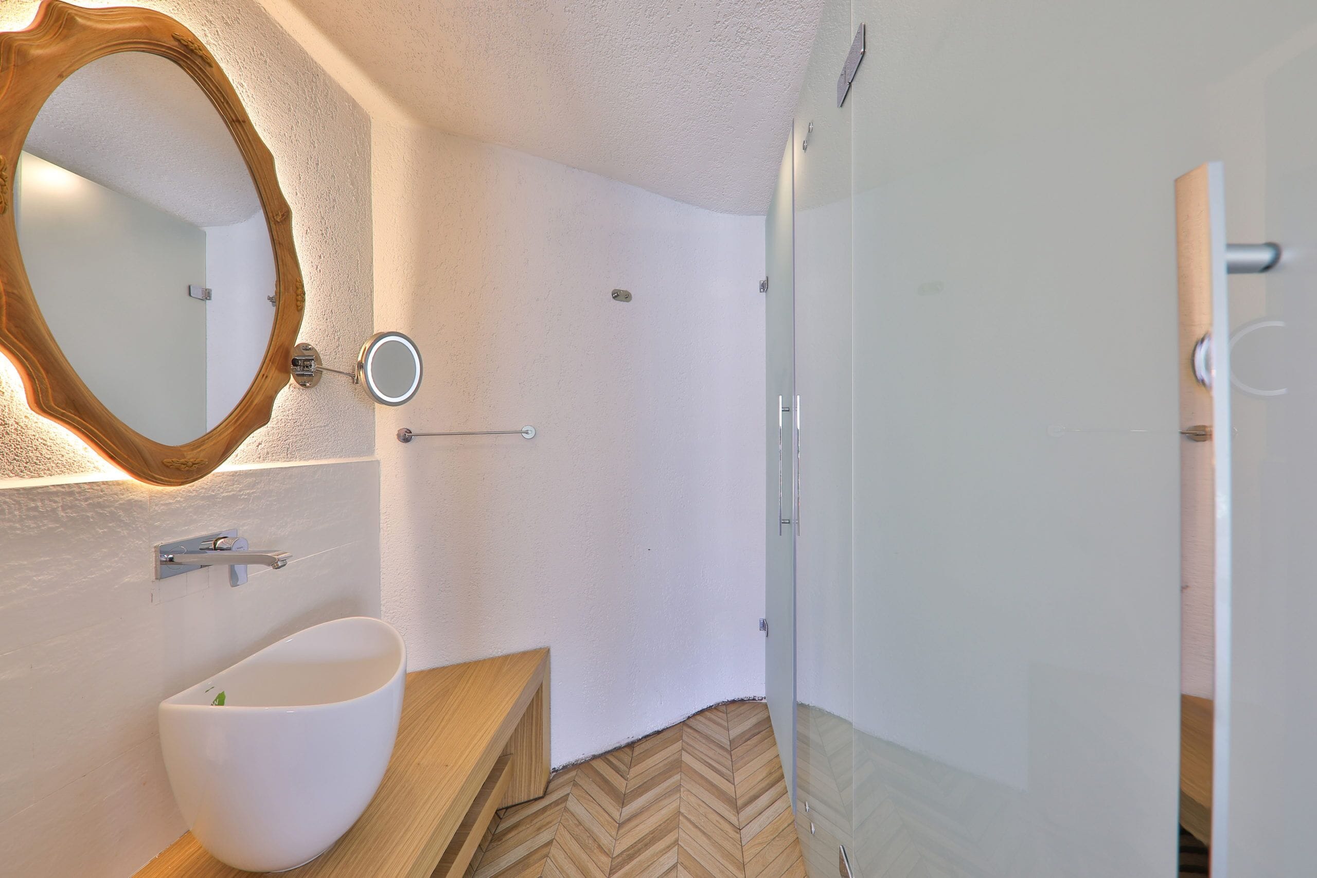 A modern bathroom with a wooden vanity, a white sink, a large mirror, and a glass shower enclosure.