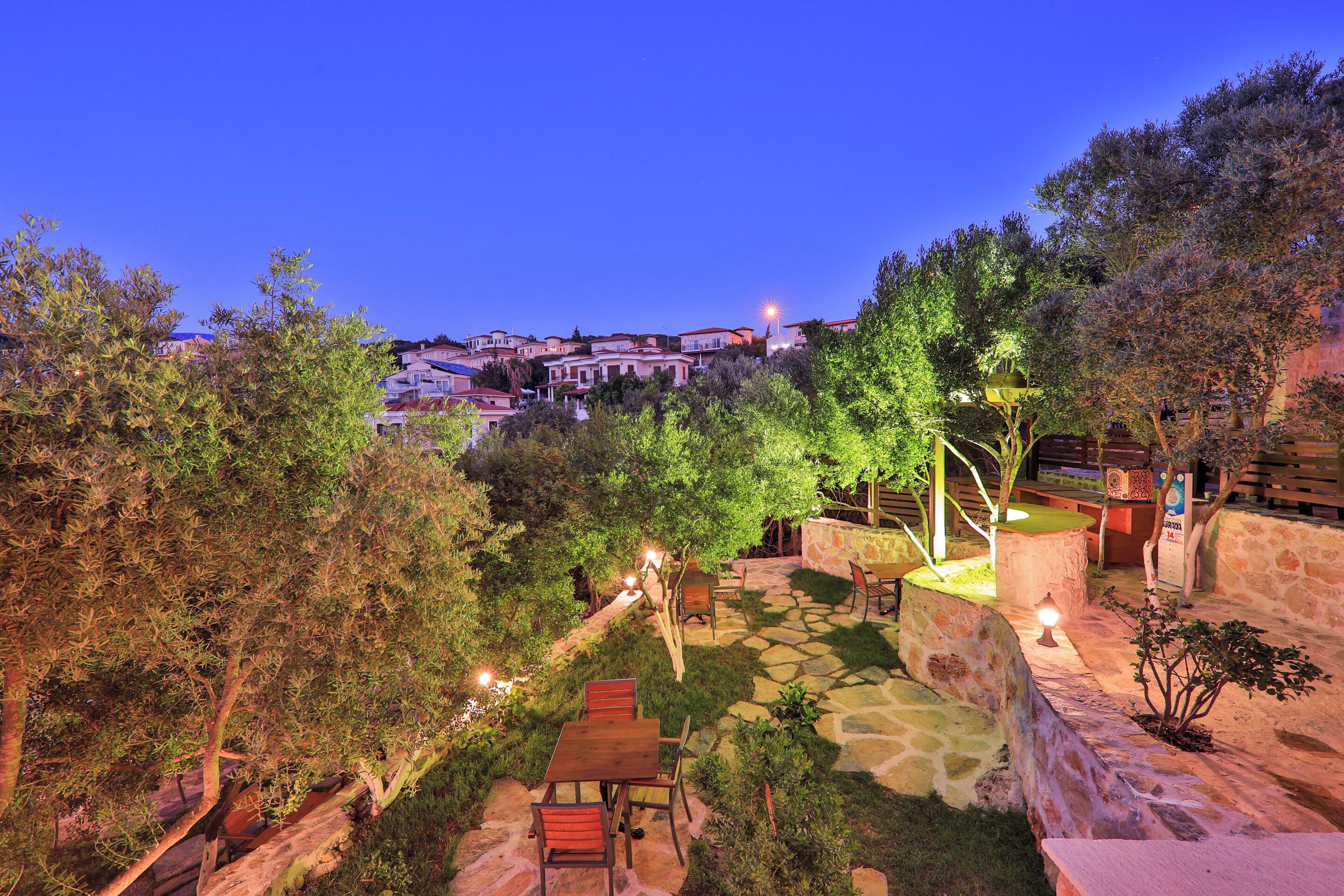 A patio area with stone flooring, wooden furniture, and a view of a hillside village at dusk.