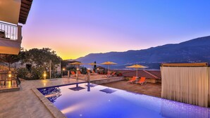 A swimming pool with a view of mountains, outdoor seating, and a covered area.