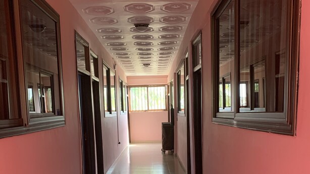 Um corredor comprido e estreito com grandes janelas em ambos os lados, piso de azulejos e teto com padrão geométrico.