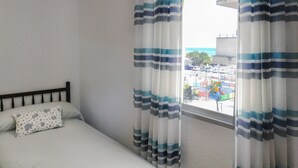 Une chambre avec un lit, une fenêtre avec des rideaux et une vue sur un parking et des immeubles.
