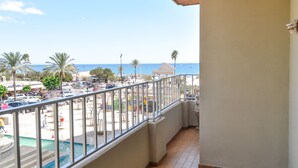 Un balcon avec vue sur une plage, des palmiers et une piscine.