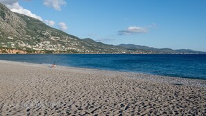 A beach with a person sunbathing, a clear sky, and a mountainous backdrop.