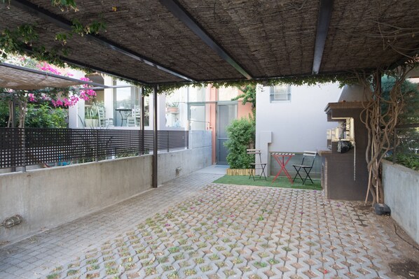 A covered patio area with a patterned tile floor, a metal fence, and a small garden with a table and chairs.